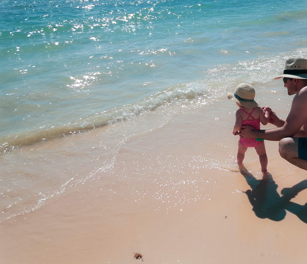 baby at beach with father standing in the waves