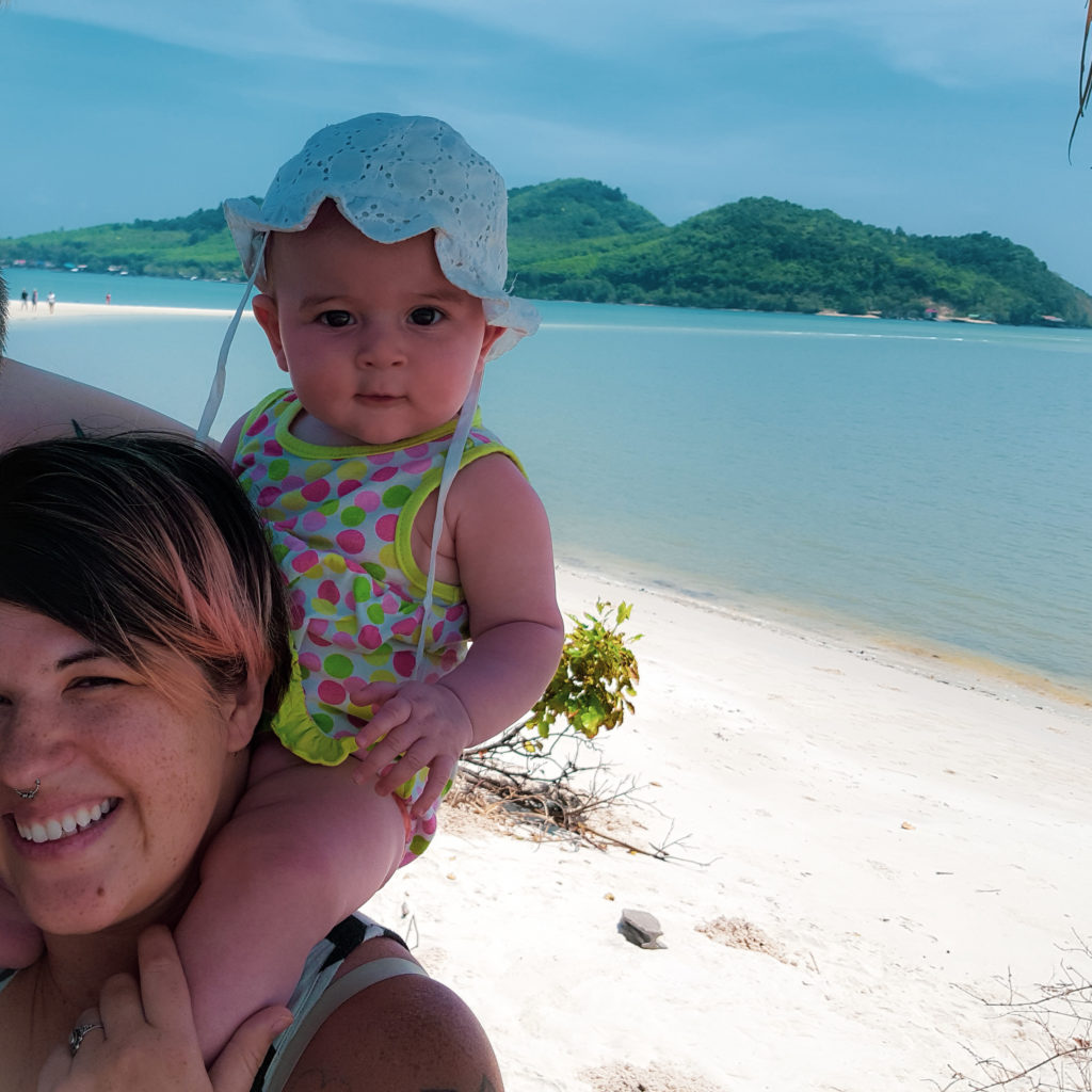 baby at the beach on mother's shoulders with island in background