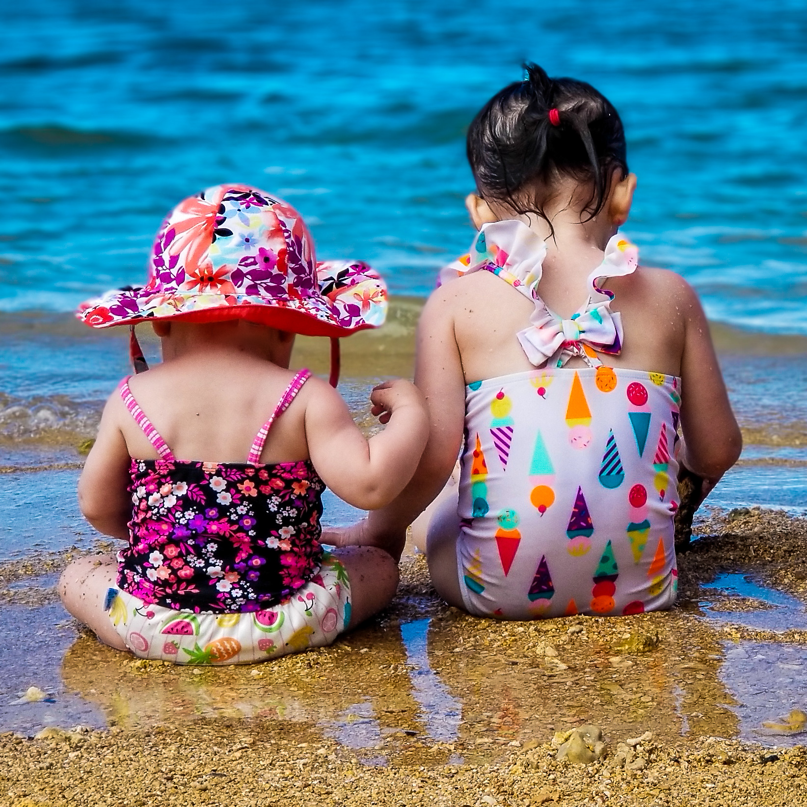 Family travel planning with baby or toddler. Two girls sitting on the beach.