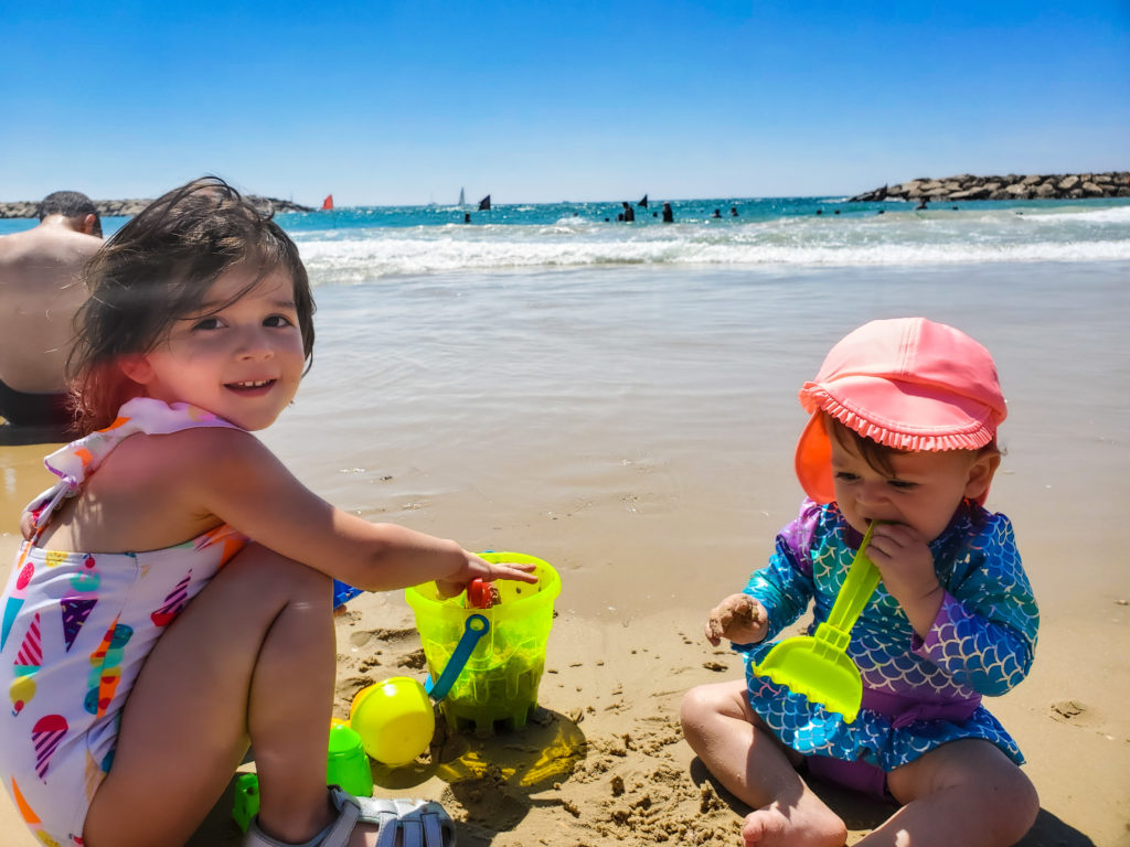toddler and baby in the sand in front of the beach in tel aviv