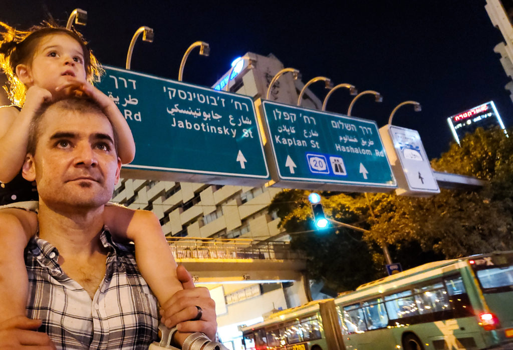 toddler on man's shoulders in front of street signs in 3 languages