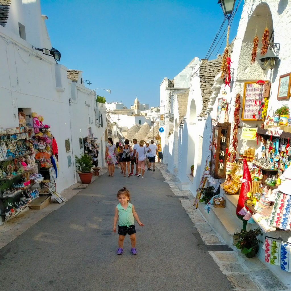 toddler in middle of pedestrian walkway surrounded by trulli shops in alberobello