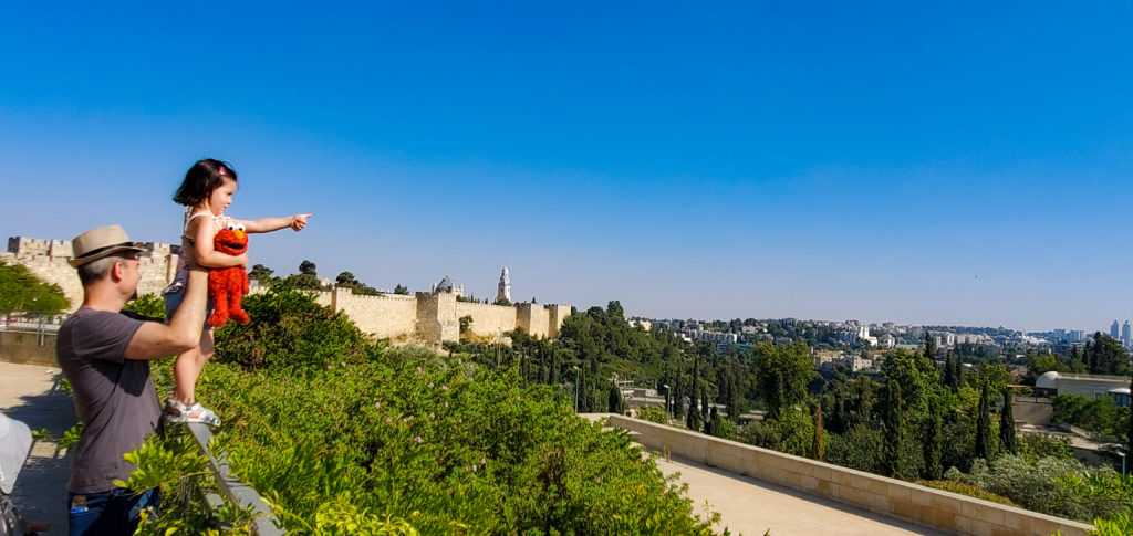 toddler in jerusalem holding elmo doll and pointing out across landscape