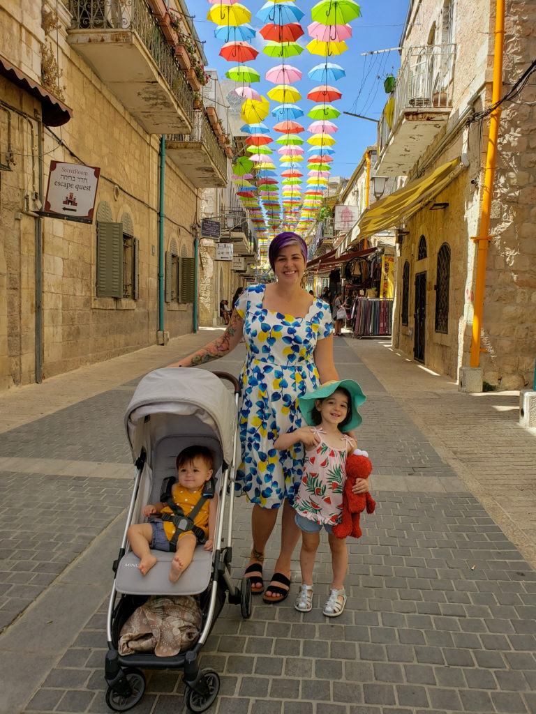 woman and toddler and baby in jerusalem under umbrella street