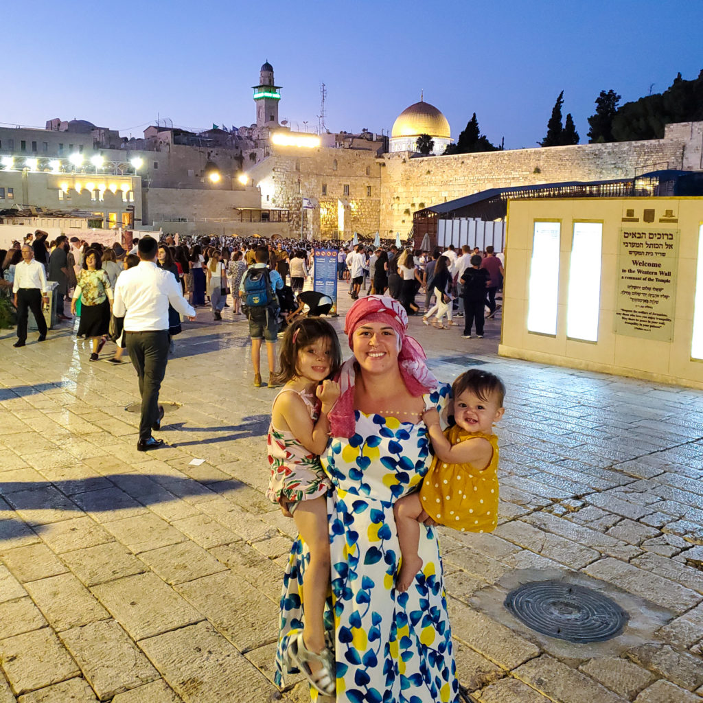 woman wearing headscarf holding toddler and baby as sun sets on western wall