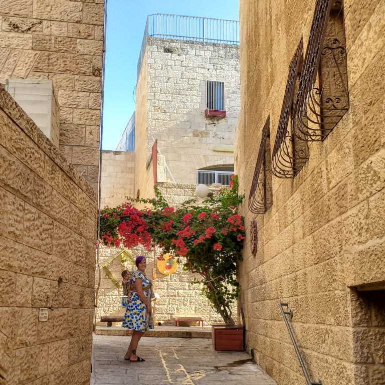 woman wearing baby on back standing under flowers in brick alley