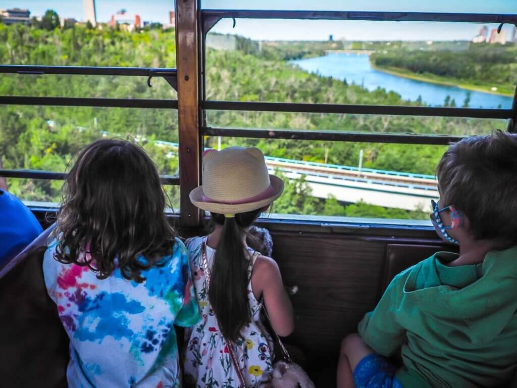three children looking out of a streetcar at a river and greenery