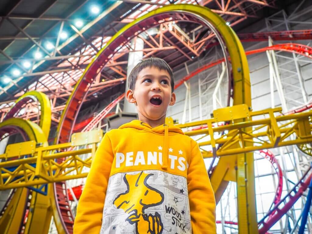 excited boy in front of indoor rollercoasters