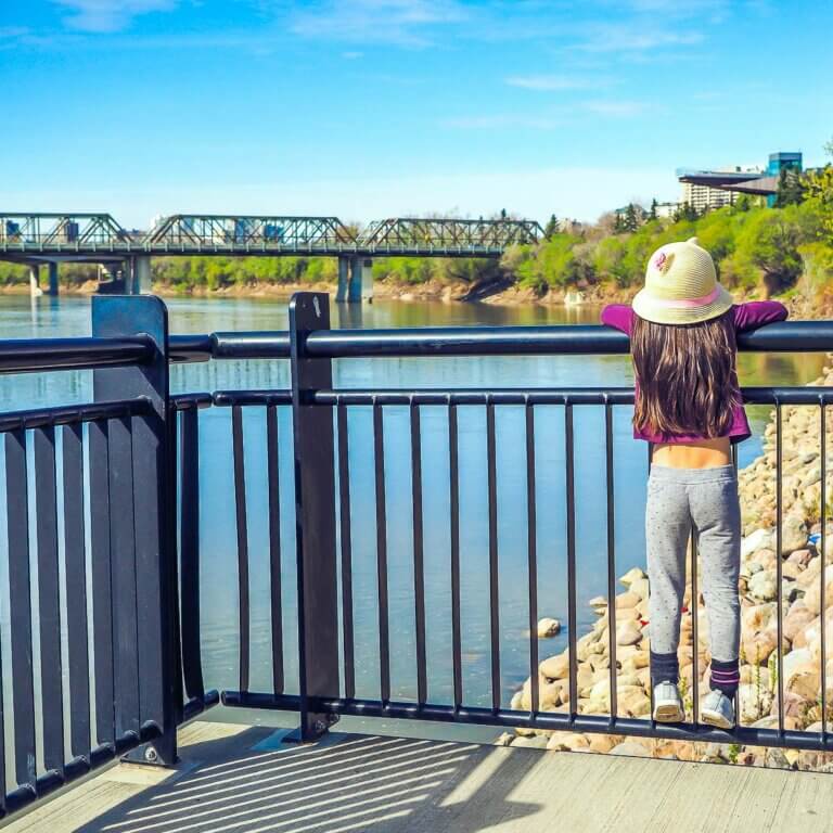 toddler in edmonton standing on railing looking out at water and bridge