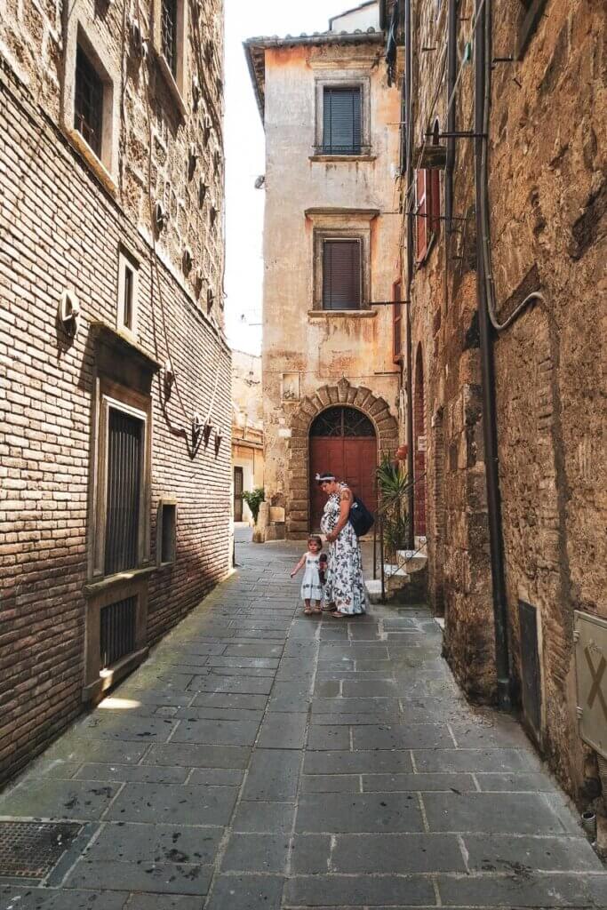 pregnant woman and child standing in alleyway between tall houses